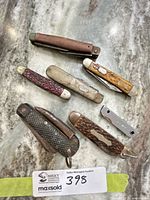 All seven folding pocket knives laid out on countertop with lot tag visible