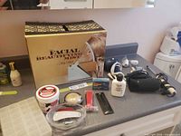 Overall view showing Lady Shick steamer box, hair dryers, curling iron, moisturizers, makeup and accessories on countertop