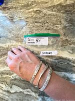 Three sterling silver bangles worn on wrist beside labelled bag