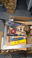 Overview of lot on box: framing square, three hand saws, tape measure, hammer, level, angle finder, bevel gauge