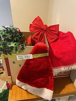 Overall view showing tree skirt, Santa hat, plastic holly, and red bow in box