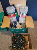 Open carton with multiple tinsel garlands and smaller box of light strings