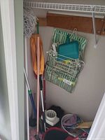 Closet view with mops, duster, broom handles, striped bag, rack, buckets and laundry basket