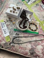 Assorted jewelry laid out including brooches, bead necklaces, bracelet, lapel pins