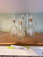 Four clear glass decanters with stoppers on shelf