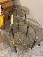 Two round smoked glass tables with brass and black legs