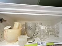 Cabinet shelf with glass etched pitcher, plastic measuring cup, syrup jug, parfait glasses