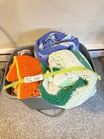 Four crocheted blankets rolled in storage bin: green-white, blue, orange-multicolour, red variant partially visible