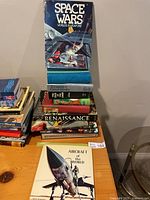 Two stacks of assorted hardcover and softcover books topped by Space Wars, Aircraft of the World in foreground
