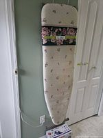 Full foldable ironing board with floral padded cover hanging on wall