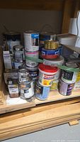Stacked assortment of paint, stain and wax cans on wooden shelf