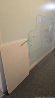 Clear plexiglass mat leaning against wall beside white cutting board