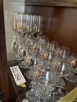 Cabinet view showing multiple port glasses and champagne flutes with Olympic logo and gold rim