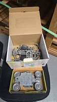 Two boxes showing barn door roller trolley and box of assorted shackles and turnbuckles