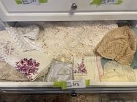 Drawer containing folded crocheted lace tablecloths, floral printed napkins, embroidered linens, doilies