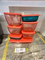 Stack of six Tupperware containers with red lids and yellow vent buttons
