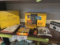 Overall view of camera, empty boxes, film and flashbulb packages on shelf