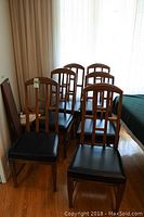 Photo showing set of six Stanley Furniture dining chairs with wooden frames and black cushioned seats, arranged in room with wooden floor and white curtains.