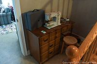 Elna sewing machine on a wooden desk with drawers beside a round stool on carpeted floor