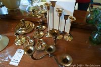 Image showing the full assortment of brass candleholders including the set of 3 tall Triad candlesticks from Ikea, multiple other brass candleholders of varying sizes and styles on a wooden surface.