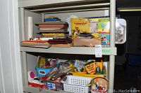 Two shelves filled with children's arts and crafts supplies including crayons, pipe cleaners, craft paper, markers, and craft books organized in baskets and containers.