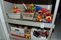 Photo showing two shelves of assorted preschool toys including various vehicles, plastic toys, and plush animal toy.