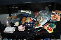 View of assorted kitchen utensils and gadgets, including bowls, rolling pins, mortar and pestle, and measuring cups arranged on a black shelf.
