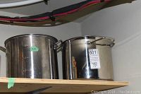 Two stainless steel stock pots on a wooden shelf, side by side, showing size and wear