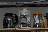 Mr. Coffee drip coffeemaker with glass carafe, stainless steel coffee percolator carafe, and Bodum French press with orange lid and handle on a shelf.