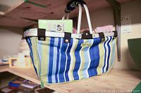 Side view of striped metal framed picnic basket showing handle and some of the paper napkins inside