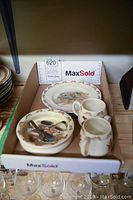 Box containing 4 pieces of Bunnykins ceramic tableware and 2 baby spoons viewed from above.