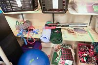 Wide shot of all items on a shelf and floor showing exercise and sporting equipment: yoga mats, racquets, jump ropes, exercise ball and step platform.