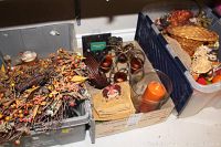 Three containers on the floor with various fall-themed decor items inside, showing artificial wreaths, a candle, small baskets, and decorative figurines.