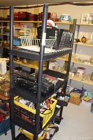 Two black plastic shelving units with various stored items, located in a cluttered storage room. Shelves show wear.