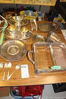 Photo showing 4 sterling silver tea spoons along with 14 silver plated serving pieces arranged on a wooden table including trays, platters, gravy boat, tongs, and bowls.