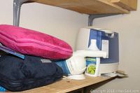 Photo showing pink and black travel pillows stacked with a handheld Dust Buster vacuum and a humidifier on a wooden shelf.
