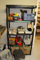 Black plastic shelving unit with multiple shelves containing assorted tools and storage bins not included in sale.