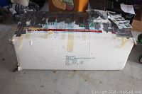 Photo of large white box with visible tape holding flaps and edges, box labeled for artificial Christmas tree, showing some wear and dirt on floor.