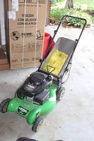 Front-left perspective showing green deck, engine housing, wheels, and attached rear grass bag