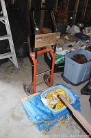 Metal hand cart with orange legs and wooden platform, assorted blue tarps and cords in a plastic container in front.
