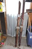 Two sets of vintage wooden downhill skis standing upright against a curtain, showing general condition and wood finish.