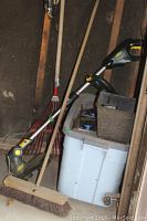 Photo showing Yardworks weed wacker with metal shaft, push broom with wooden handle and red leaf rake, plastic bin in background