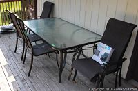 Overall view: glass-top rectangular patio table with six dark brown mesh sling chairs on deck