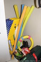 Three yellow paddle boards with blue polka-dot covers standing vertically among colorful foam water noodles and other aquatic accessories.