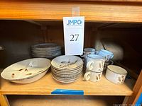 View of stacked dinner plates, serving bowls, mugs and saucers on shelf