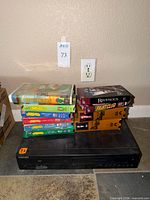 Samsung DVD-V9800 combo player with stack of eight VHS tapes including Fight Club, Ravenous, Pete's Dragon and four children’s titles