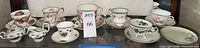 Entire lot arranged on shelf showing seven teacup and saucer sets with sugar and creamer
