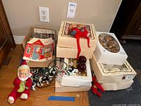 Group shot showing boxed ornaments, string lights, Santa doll, elves, greeting booklet