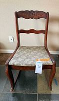 Front view of wooden rocking chair showing carved crest rail and upholstered seat