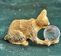 Side view of gold-tone metal cat figurine holding clear faceted crystal ball